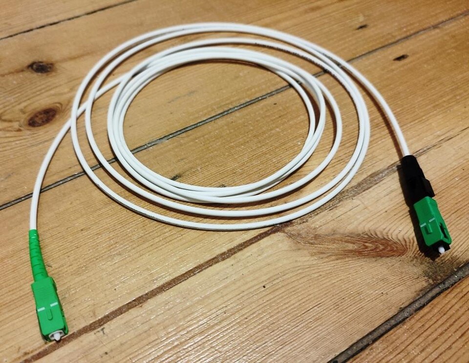An SC-APC fiber optic cable with a green angled-polish connector, showing the thin glass fiber core inside the yellow single-mode jacket